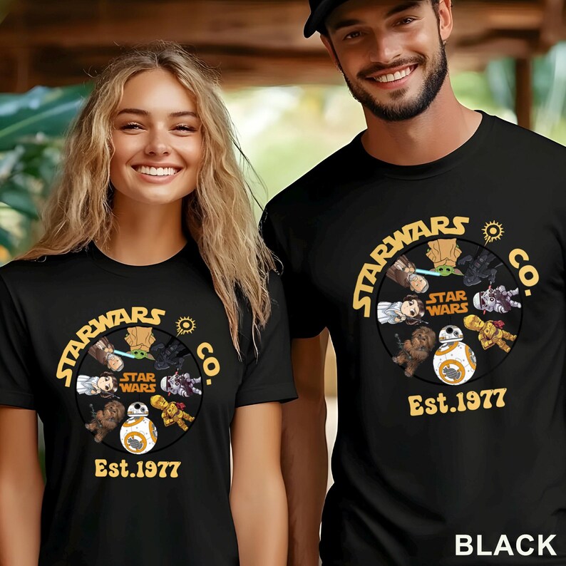 Peut inclure: T-shirts noirs avec un motif Star Wars. Le motif comprend le texte "STARWARS CO." et "Est.1977" ainsi que divers personnages de Star Wars. Les t-shirts sont port&eacute;s par deux personnes.