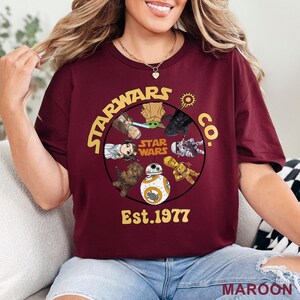 Peut inclure: T-shirt bordeaux avec un motif circulaire de personnages de Star Wars et le texte "STARWARS CO. STAR WARS Est.1977". Le motif comprend Yoda, Dark Vador et BB-8. Le mot "MAROON" est imprim&eacute; en bas.