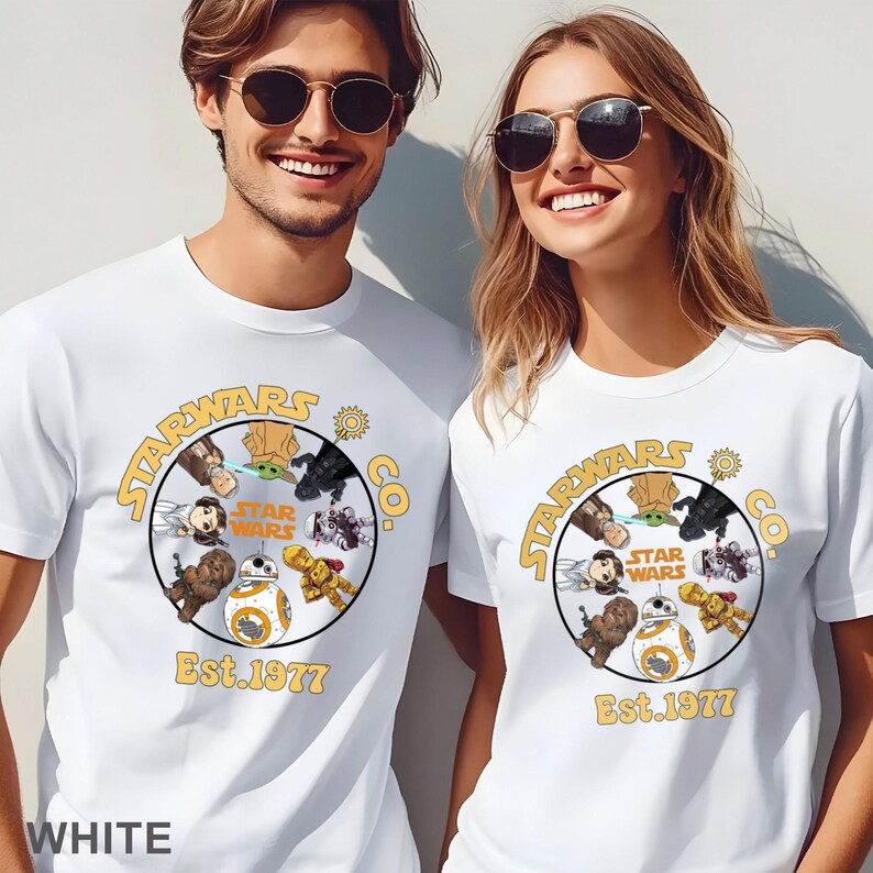 Peut inclure: T-shirts blancs avec un motif circulaire repr&eacute;sentant des personnages de Star Wars et le texte "STARWARS CO." et "Est. 1977" en jaune. Le motif comprend des personnages comme BB-8 et Yoda.