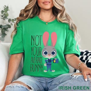 Puede incluir: Camiseta verde irland&eacute;s con el texto "NOT YOUR AVERAGE BUNNY" y un personaje de conejo de dibujos animados con uniforme de polic&iacute;a. El conejo tiene orejas rosas y sostiene un malet&iacute;n y una linterna.