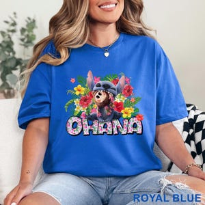 May include: Royal blue t-shirt featuring a graphic of Stitch from Lilo & Stitch surrounded by colorful flowers. The word "OHANA" is printed in a floral font. The shirt is a vibrant blue.