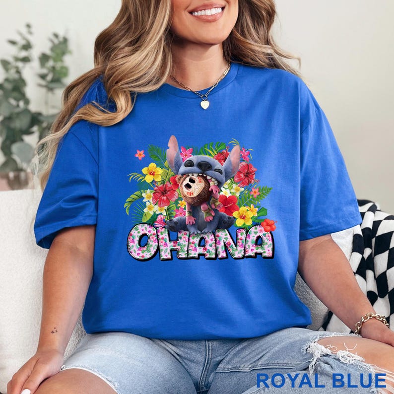May include: Royal blue t-shirt featuring a graphic of Stitch from Lilo & Stitch surrounded by colorful flowers. The word "OHANA" is printed in a floral font. The shirt is a vibrant blue.