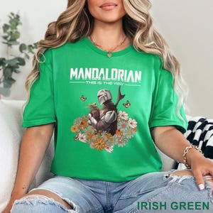 May include: Irish green t-shirt featuring a graphic of The Mandalorian and Grogu surrounded by flowers and butterflies. The text "MANDALORIAN - THIS IS THE WAY" is printed across the top.