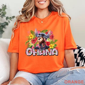 May include: Orange t-shirt featuring a colorful graphic of Stitch and a koala bear surrounded by tropical flowers. The word "OHANA" is printed in a playful font. The shirt is a vibrant orange color.
