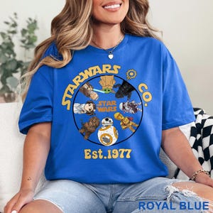 Peut inclure: T-shirt bleu royal avec un motif circulaire Star Wars, avec des personnages et le texte "STARWARS CO. Est. 1977". Le design comprend Yoda, BB-8 et d'autres personnages. Le t-shirt est bleu vif.