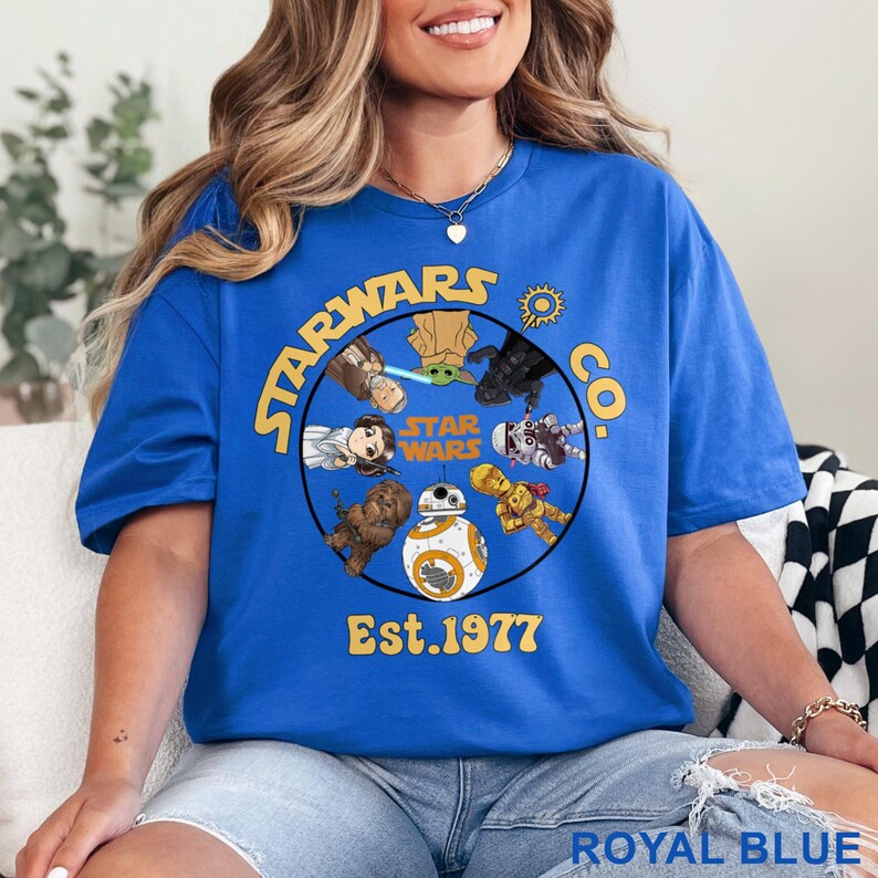 Peut inclure: T-shirt bleu royal avec un motif circulaire Star Wars, avec des personnages et le texte "STARWARS CO. Est. 1977". Le design comprend Yoda, BB-8 et d'autres personnages. Le t-shirt est bleu vif.