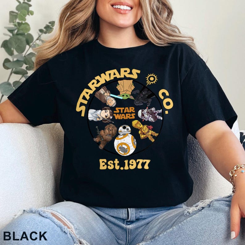 Peut inclure: T-shirt noir avec un motif circulaire jaune repr&eacute;sentant des personnages de Star Wars et le texte "STARWARS CO. Est. 1977". Le design comprend des personnages comme Yoda et BB-8 de la franchise Star Wars.