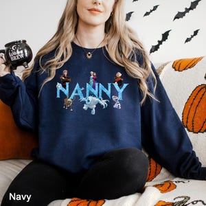 Op de afbeelding: Marineblauwe sweatshirt met het woord "Nanny" in een lichtblauwe letter, met cartoonfiguren. De sweatshirt heeft een ronde hals. Het woord "Navy" staat linksonder in de afbeelding.