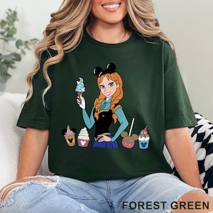May include: Forest green t-shirt featuring a cartoon of a character with red hair and a blue dress holding an ice cream cone. The shirt also has images of ice cream cones and the text "FOREST GREEN".