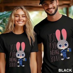 Puede incluir: Camisetas negras con un dise&ntilde;o de conejo de dibujos animados y el texto "NOT YOUR AVERAGE BUNNY". El conejo tiene orejas rosas, un uniforme azul y un malet&iacute;n. La palabra "BLACK" est&aacute; en la parte inferior.