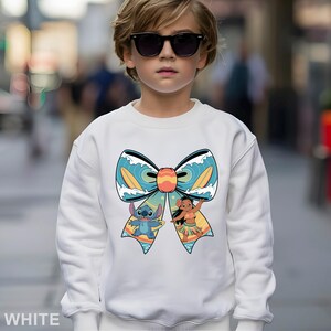 Puede incluir: Sudadera blanca con un gran dise&ntilde;o de lazo con dibujos animados de Stitch y Lilo. El lazo tiene un patr&oacute;n de olas azules y amarillas con tablas de surf. Una sudadera c&oacute;moda e informal.