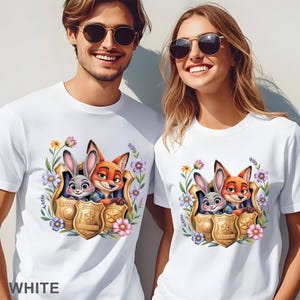 Puede incluir: Camisetas blancas con un gr&aacute;fico colorido de los personajes de Zootopia, Judy Hopps y Nick Wilde, dentro de una placa de polic&iacute;a, rodeados de flores. La palabra "WHITE" est&aacute; impresa en la parte inferior.