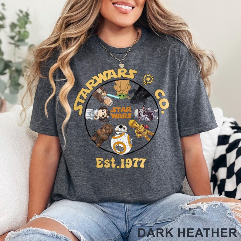 Peut inclure: T-shirt gris fonc&eacute; avec un motif circulaire repr&eacute;sentant des personnages de Star Wars et le texte "STARWARS CO. Est. 1977". Le design comprend des personnages comme Yoda et BB-8 de la franchise Star Wars.