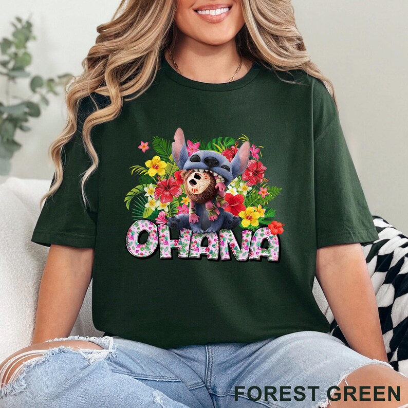 May include: Forest green t-shirt featuring a cartoon character with a floral design and the word "OHANA". The character is wearing a mask and surrounded by colorful flowers. The shirt is a dark green color.