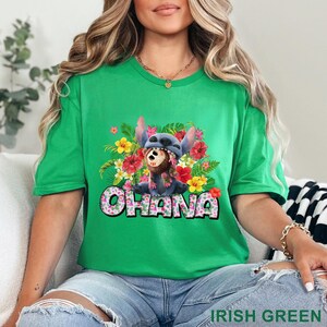 May include: Irish green t-shirt featuring a graphic of Stitch from Lilo & Stitch, wearing a floral lei and surrounded by flowers. The word "OHANA" is displayed in a floral font. The shirt is a short-sleeved crew neck.