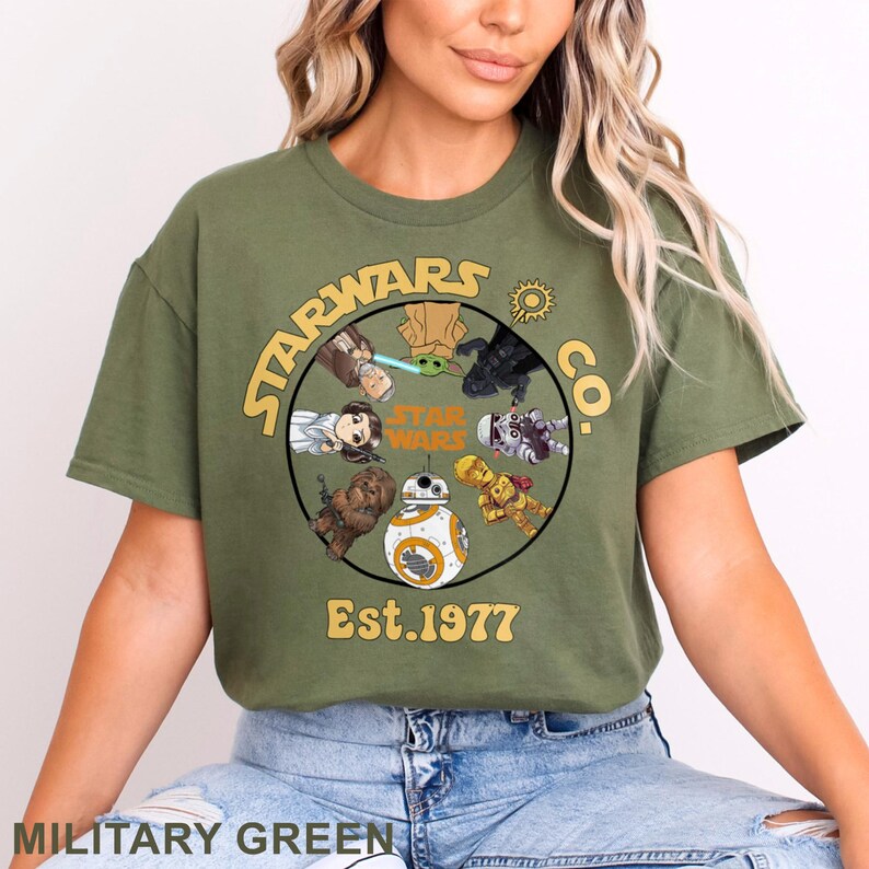 Peut inclure: T-shirt vert militaire avec un motif circulaire repr&eacute;sentant des personnages de Star Wars et le texte "STARWARS CO." et "Est.1977". Le motif comprend des personnages comme Dark Vador, BB-8 et Chewbacca. Le t-shirt est de couleur unie.