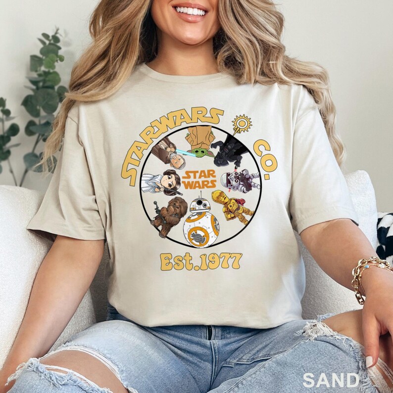 Peut inclure: T-shirt couleur sable avec un motif circulaire repr&eacute;sentant des personnages de Star Wars et le texte "STARWARS CO. Est. 1977." Le design comprend des personnages comme Chewbacca, BB-8 et Dark Vador. C'est un v&ecirc;tement d&eacute;contract&eacute;.