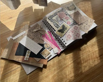 Könnte beinhalten: Ein Scrapbook mit einer Vielzahl von Dekorpapieren, Bändern und Verzierungen. Das Scrapbook ist geöffnet und zeigt eine Seite mit einem Schmetterling, einem Kompass und anderen dekorativen Elementen. Das Scrapbook liegt auf einer Holzoberfläche.
