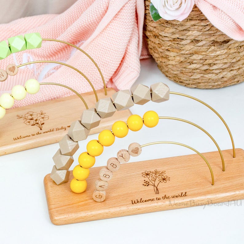Puede incluir: &Aacute;baco de madera para beb&eacute;s con arcos dorados y cuentas de colores. La base est&aacute; grabada con "Welcome to the world" y un dise&ntilde;o floral. Algunas cuentas deletrean "GABBY". Dise&ntilde;ado para el aprendizaje temprano.