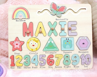 May include: Wooden puzzle board featuring the name "MAXIE" in colorful, raised letters. Includes shapes, numbers 1-10, a rainbow, and a butterfly. The board is designed for educational play and early learning.