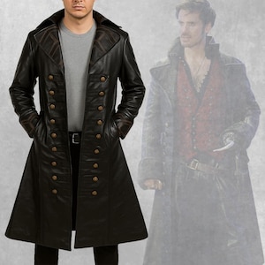 Puede incluir: Un abrigo largo de cuero negro con diseño cruzado y botones dorados. El abrigo presenta un cuello ancho y lo lleva una persona. El abrigo tiene un corte entallado y un bajo acampanado.