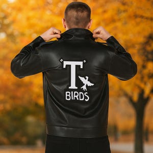 May include: Black leather jacket with a white "T Birds" patch on the back. The jacket has a classic design with a collar and a front zipper. The patch features a stylized "T" and a bird graphic.