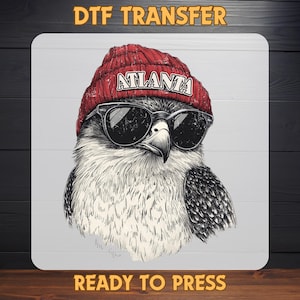 May include: A graphic illustration of a hawk wearing sunglasses and a red beanie with the word "ATLANTA" on it. The image is labeled "DTF TRANSFER" at the top and "READY TO PRESS" at the bottom.