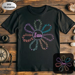 May include: Black t-shirt with a floral design featuring the words "I am" in a circle, surrounded by positive affirmations like "brave," "capable," and "amazing." The shirt has a crew neck and short sleeves.