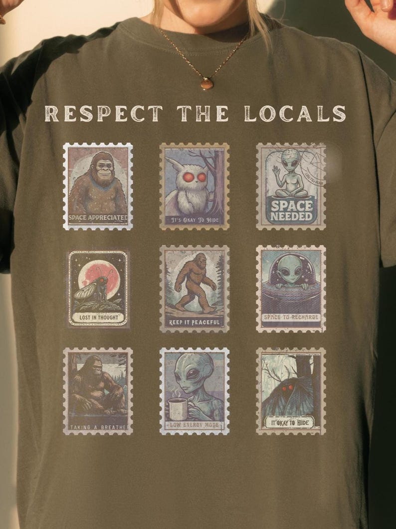 A Pepper colored Comfort Colors t-shirt with "Respect The Locals" cryptid stamp graphic, featuring Bigfoot, Mothman, and Alien stamps. Ideal for cryptid lovers and introverts.