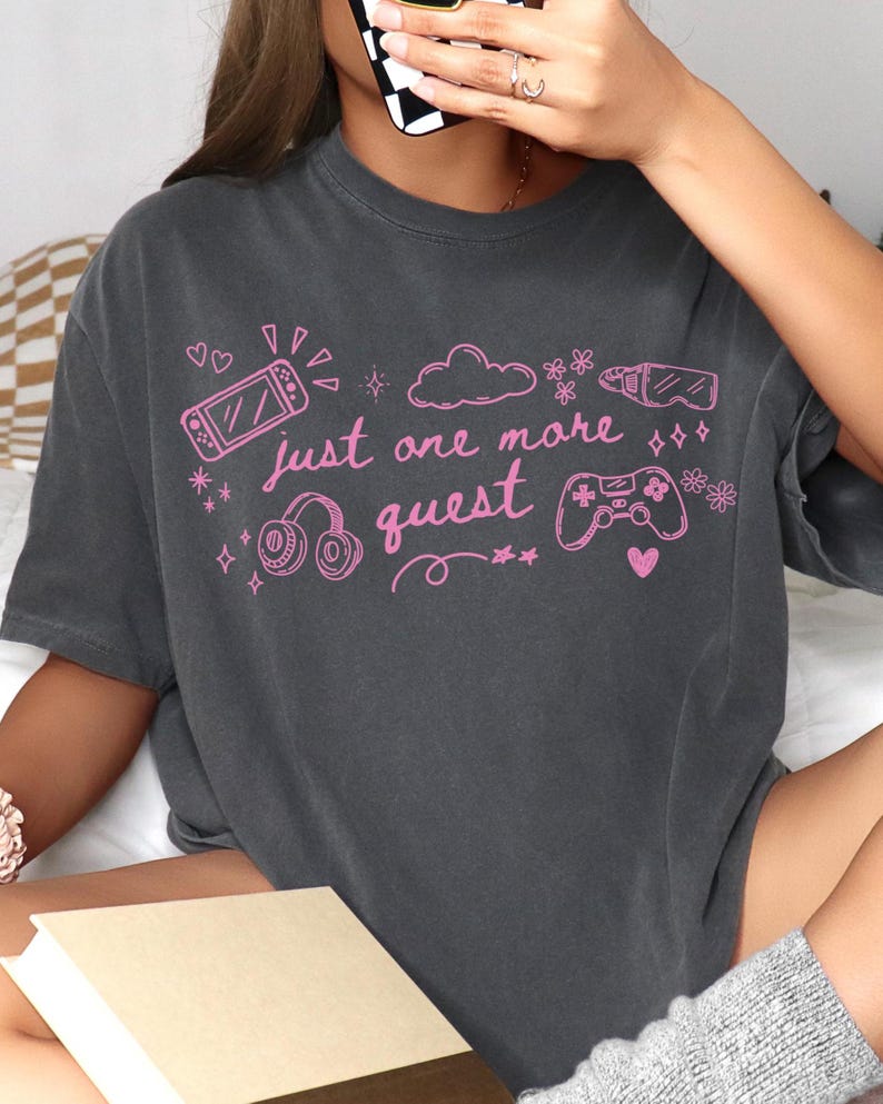 Dark gray cozy gamer aesthetic shirt with pink graphic text just one more quest worn in relaxed indoor setting