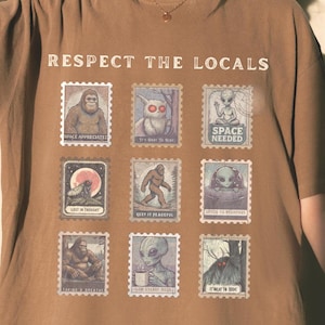 An Espresso colored Comfort Colors t-shirt with "Respect The Locals" cryptid stamp graphic, featuring Bigfoot, Mothman, and Alien stamps. Ideal for cryptid lovers and introverts.