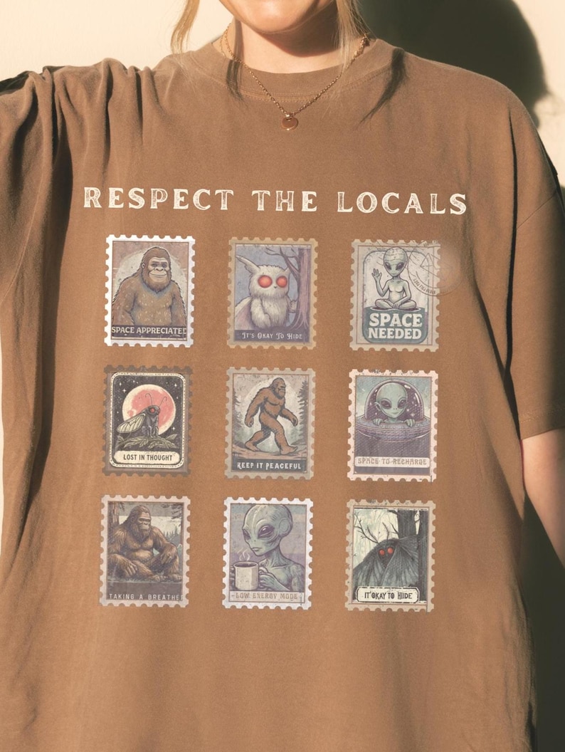 An Espresso colored Comfort Colors t-shirt with "Respect The Locals" cryptid stamp graphic, featuring Bigfoot, Mothman, and Alien stamps. Ideal for cryptid lovers and introverts.