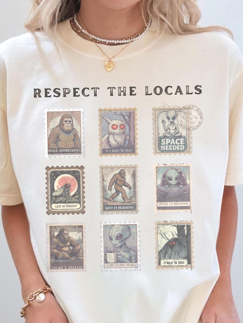 An Ivory colored Comfort Colors t-shirt with "Respect The Locals" cryptid stamp graphic, featuring Bigfoot, Mothman, and Alien stamps. Ideal for cryptid lovers and introverts.