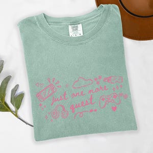 Cozy gamer girl shirt on sage green Comfort Colors tee with pink just one more quest graphic and gaming doodles