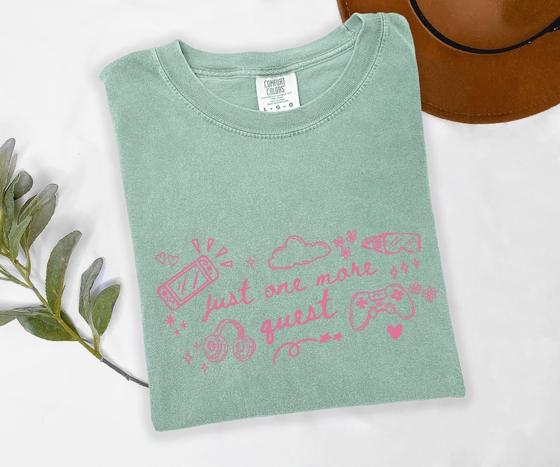Cozy gamer girl shirt on sage green Comfort Colors tee with pink just one more quest graphic and gaming doodles
