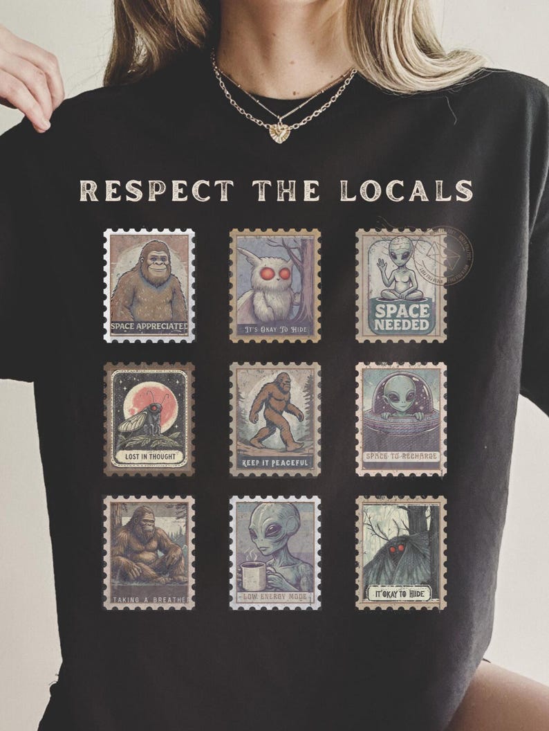 A black Comfort Colors t-shirt with "Respect The Locals" cryptid stamp graphic, featuring Bigfoot, Mothman, and Alien stamps. Ideal for cryptid lovers and introverts.