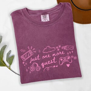 Cute gamer aesthetic shirt on berry purple Comfort Colors tee featuring pink gaming graphic and just one more quest phrase
