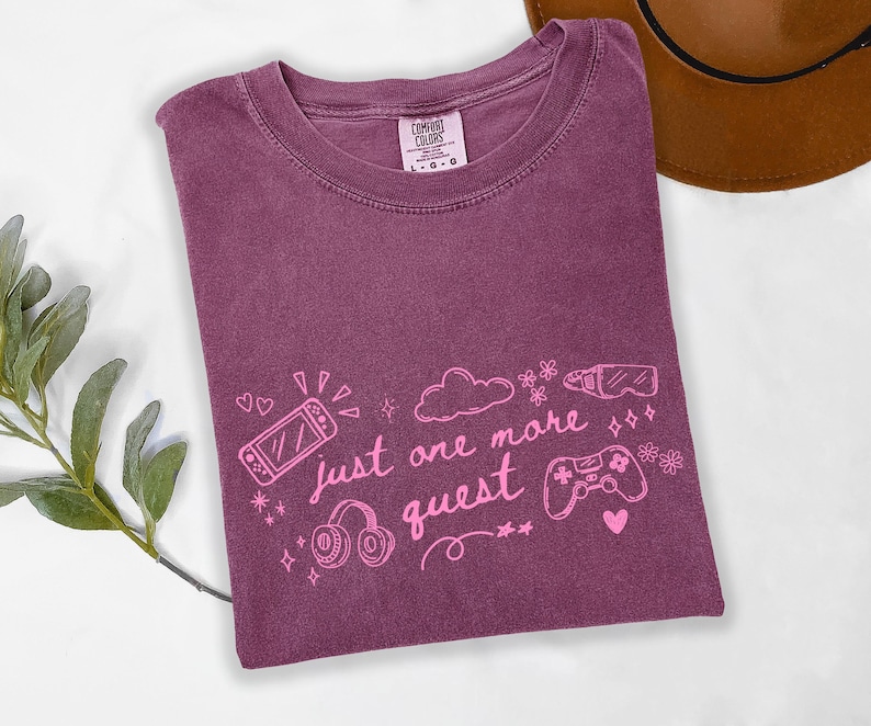 Cute gamer aesthetic shirt on berry purple Comfort Colors tee featuring pink gaming graphic and just one more quest phrase