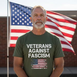 May include: An olive green t-shirt with the text "VETERANS AGAINST FASCISM" in white, along with a distressed American flag graphic. An American flag waves in the background.