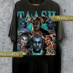 May include: Black t-shirt with a graphic of several blue-skinned figures wearing elaborate headwear. The word "TAASH" is printed across the top in teal. The shirt has a vintage, worn appearance.