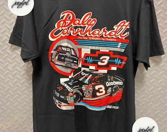 May include: Black t-shirt featuring a colorful graphic of a race car with the number 3 and the name Dale Earnhardt. The design includes the words "Five Time Winston Cup Champion". The shirt has a classic crew neck.