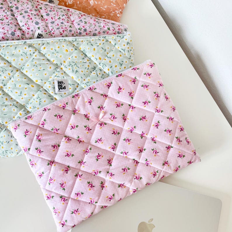 May include: Three quilted fabric laptop sleeves with floral patterns. The sleeves are in shades of pink, green, and brown. The text "He + She" is visible on the green sleeve.