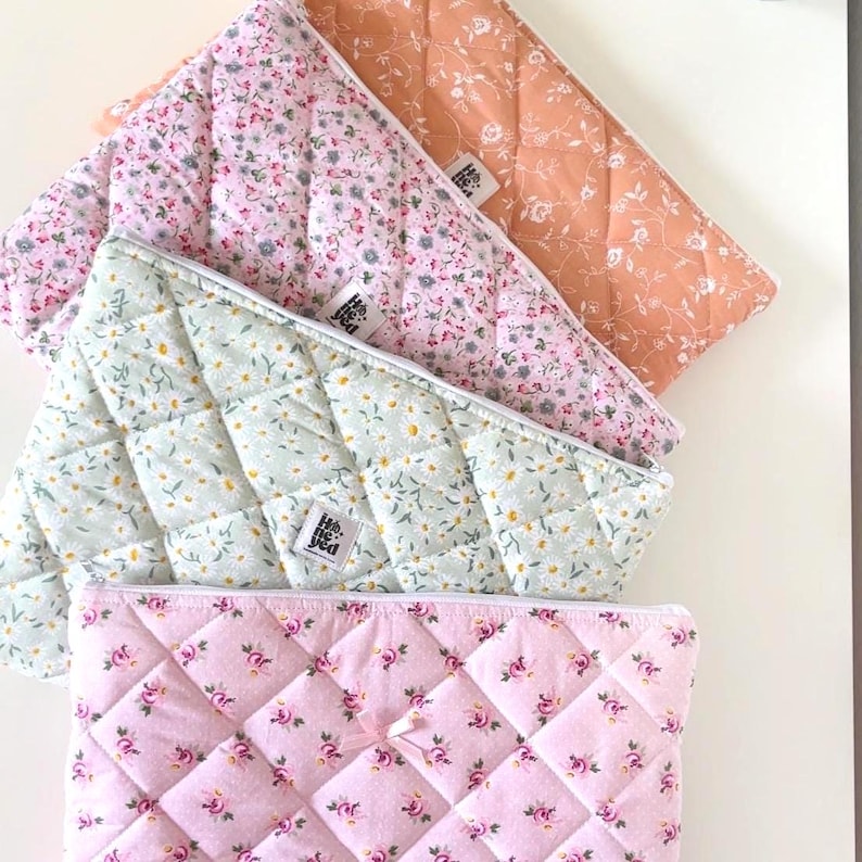 May include: Four quilted fabric pouches with floral patterns. The pouches are in shades of pink, green, and orange. The pouches have white piping and a white label with the text "Hello You" on them.