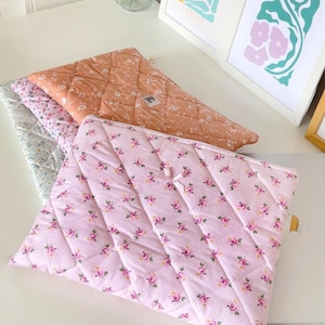 May include: Three quilted fabric pouches with floral patterns. The top pouch is orange with white flowers, the middle pouch is light blue with white flowers, and the bottom pouch is pink with small pink flowers.