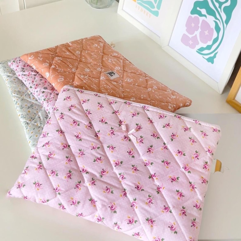May include: Three quilted fabric pouches with floral patterns. The top pouch is orange with white flowers, the middle pouch is light blue with white flowers, and the bottom pouch is pink with small pink flowers.