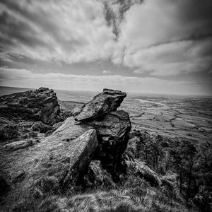 May include: A black and white photograph of a rocky landscape with a dramatic sky. The rocks are jagged and weathered, and the sky is filled with dark clouds. The scene is reminiscent of a wild and rugged landscape.