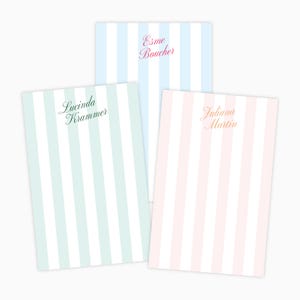 May include: Three personalized notepads with vertical stripes in pastel colors: light blue, mint green, and pink. Each notepad features a different name in elegant script: Esme Boucher, Lucinda Krammer, and Juliana Martin. The notepads are arranged on a white background.