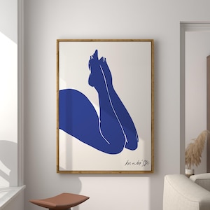 Può includere: Una stampa artistica incorniciata con un'illustrazione blu minimalista delle gambe e del busto di una persona. L'opera d'arte è ambientata su uno sfondo color crema e incorniciata in legno naturale. La firma dell'artista è in basso a destra.