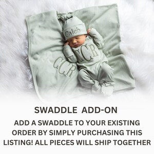 May include: A green swaddle blanket with the name "Caleb" embroidered on it. The swaddle is shown with a matching green baby outfit and hat.