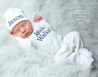May include: A newborn baby wearing a white hat and footed onesie, both embroidered with the name "Jason" and "Jason Walker" in navy blue. The outfit has fold-over mittens and can be worn footed or non-footed. The baby is lying on a fluffy white surface.